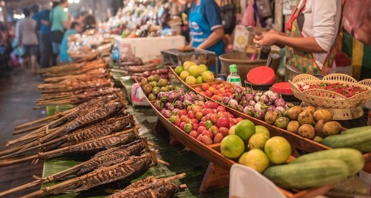 Food market with a variety of colorful vegetables and grilled fish on display.
