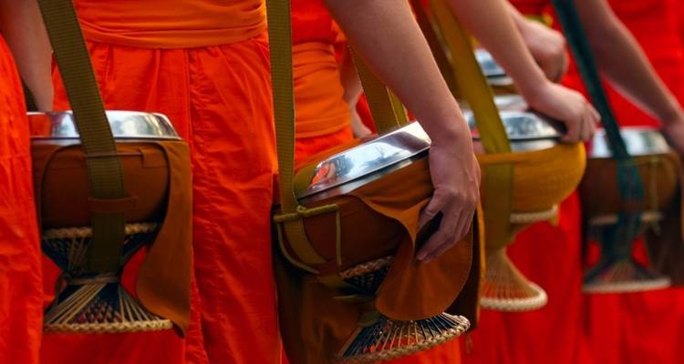 Cropped image of people in vibrant orange robes carrying offering bowls.