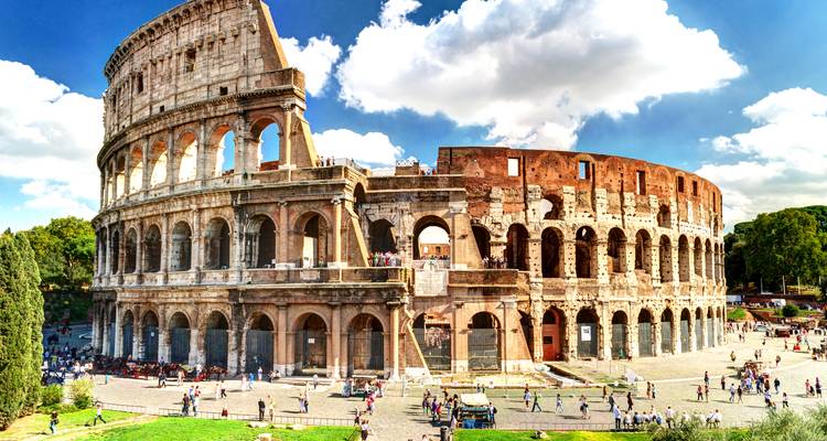Iconic Colosseum in Rome bathed in sunlight with crowds of visitors around its base.