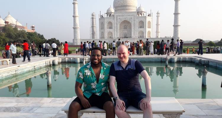 Deux voyageurs sont assis sur un banc en marbre près du bassin de réflexion face au Taj Mahal