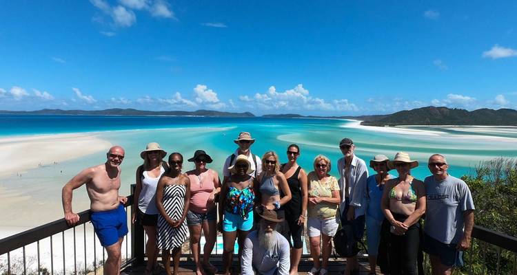Un groupe de personnes posant sur un point de vue avec une vue sur des plages de sable blanc et des eaux turquoise.