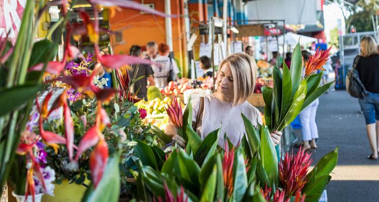 Vrouw selecteert tropische bloemen bij een levendige buitenmarktstand.