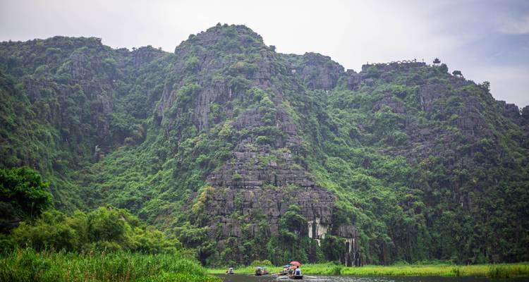 Weelderige groene karstheuvels met boten en een vredige rivier op de voorgrond.
