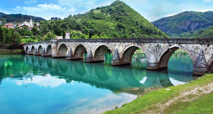 Historische Brücke über einem türkisfarbenen Fluss mit grünen Hügeln.