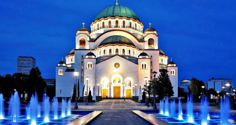 A grand cathedral with fountains illuminated at night.