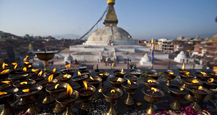 Brennende Öllampen mit einer Stupa im Hintergrund unter klarem Himmel.