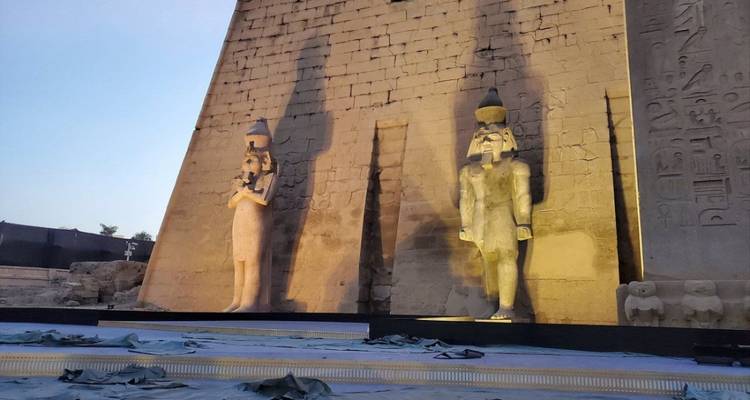Estatuas del antiguo Egipto frente a un gran pilono al atardecer.
