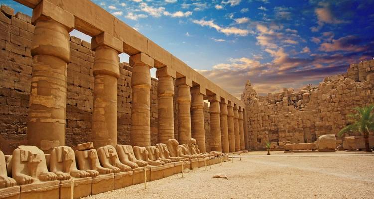 Oude Egyptische ruïnes met zuilen en standbeelden onder een levendige hemel.