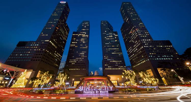 Nachtszene des Brunnens des Reichtums in Suntec City mit Lichtschweifen und aufragenden Bürogebäuden.