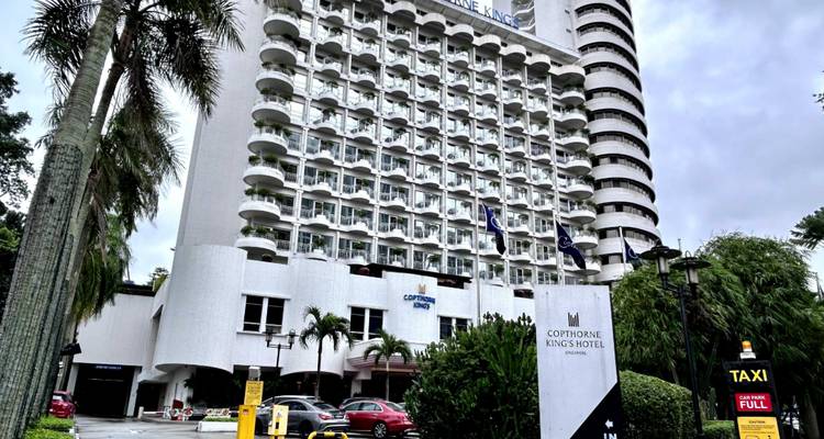 Das Copthorne King's Hotel Singapore, umrahmt von Palmen an einem bewölkten Tag.