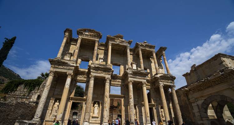 Ruines antiques avec de hautes colonnes et des sculptures détaillées sous un ciel bleu clair.