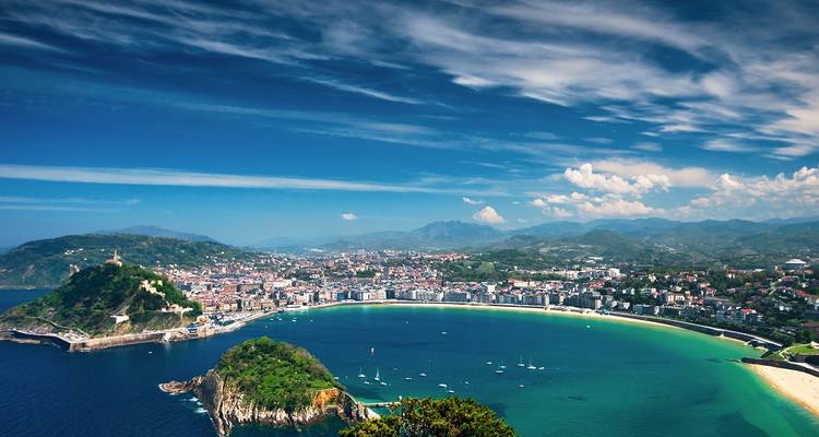 Panoramablick über die türkisfarbene Sichel der Bucht La Concha und die Stadtsilhouette von San Sebastian unter einem lebhaften blauen Himmel.
