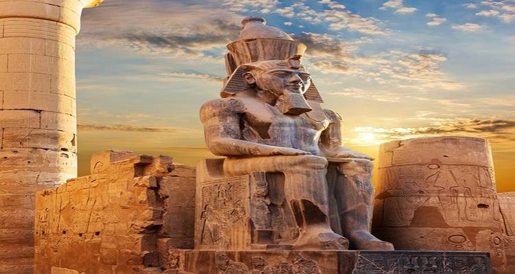 Statue eines antiken Pharaos vor Tempelsäulen bei Sonnenuntergang.