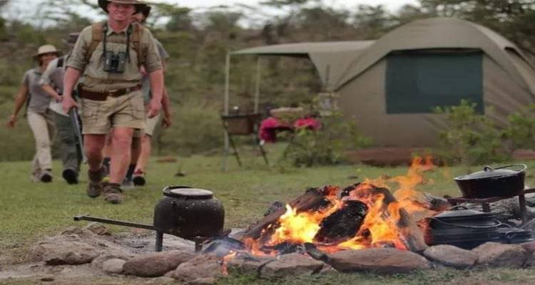 Eine Gruppe von Campern, die in der Nähe eines Zeltes und eines Lagerfeuers gehen.