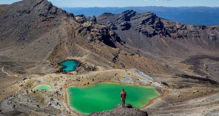 Hiker overlooking the vibrant colored lakes in a volcanic landscape.