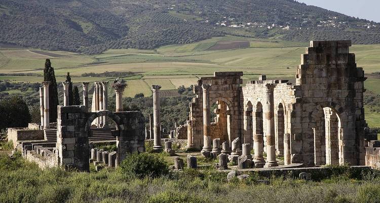 Ancient Roman ruins with a backdrop of rolling green hills.