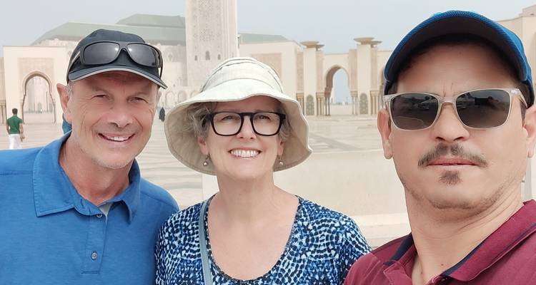Three people smiling in front of a mosque with arches and domes.