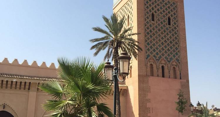 Hoher Moscheenturm mit kunstvollem Design und Palme.