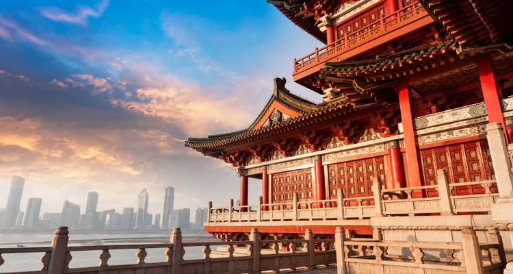 Architecture chinoise traditionnelle surplombant un horizon de ville moderne au coucher du soleil.