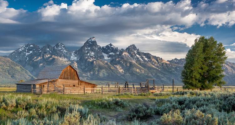 Grange historique avec un arrière-plan montagneux spectaculaire sous un ciel partiellement nuageux.