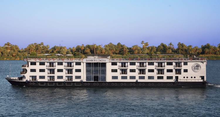 Modern Nile cruise ship sails past palm-fringed banks under a clear purple-blue sky.