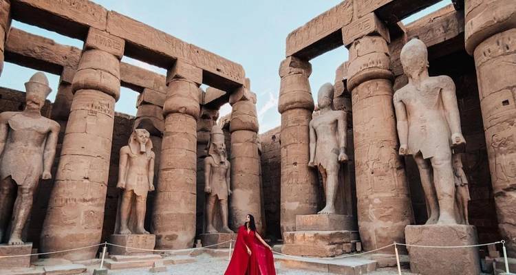 Una mujer con un vestido rojo entre grandes columnas antiguas.