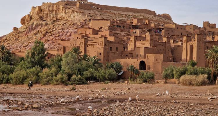 Kasbah emblématique d'Ait Benhaddou avec végétation à la base et fort au sommet de la colline.