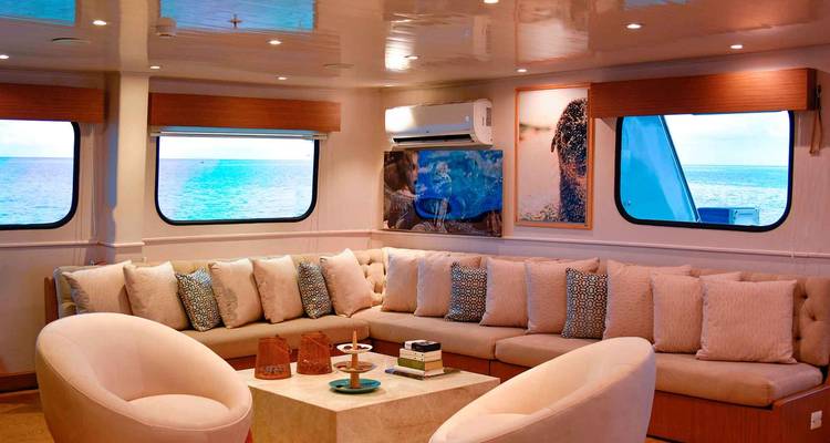 Salón elegante con asientos acolchados, decoración moderna y vistas al mar a través de grandes ventanales.