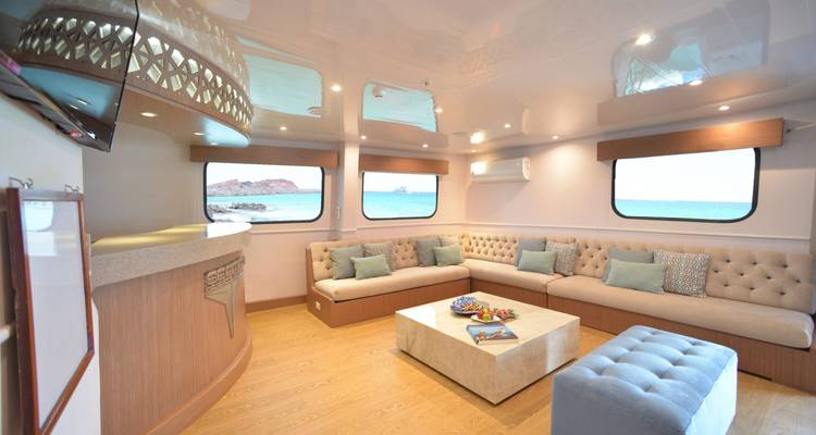 Acogedora sala de estar del barco con asientos beige, mesa baja y vistas amplias del agua afuera.