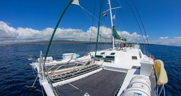 Cubierta delantera del catamarán con camas elásticas y vistas al océano bajo un cielo parcialmente nublado.