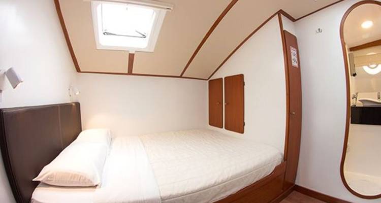 Cabina compacta con una cama doble, tragaluz y acabados de madera minimalista.