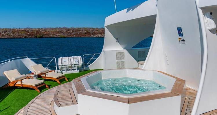 Open dek met jacuzzi en ligstoelen met uitzicht op het water.