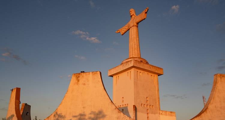 A large Christ the King statue on a hill during sunset.