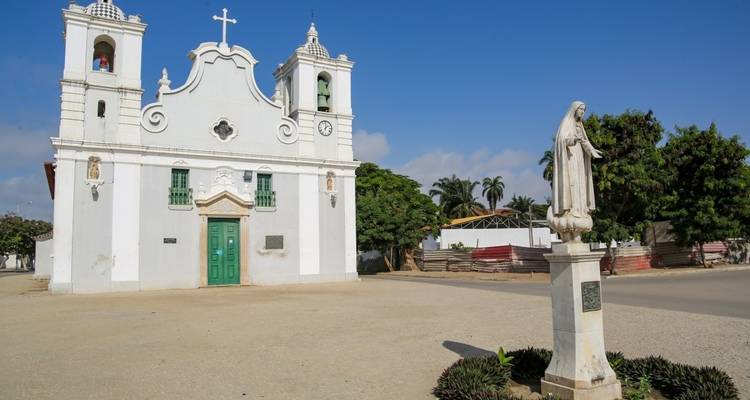 A white colonial-style church with a statue in the front yard.