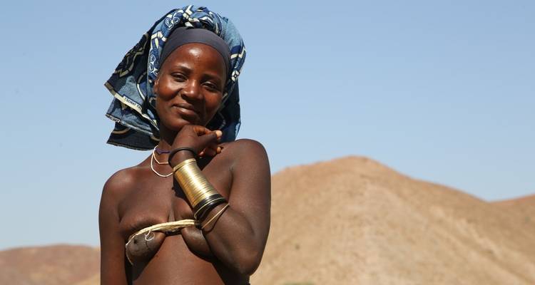 A woman standing in a desert landscape wearing traditional arm jewelry.