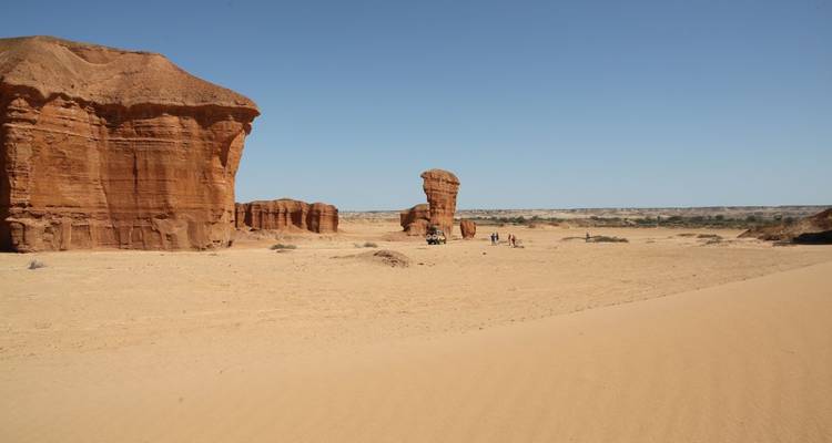 Des gens marchant près de grandes formations rocheuses dans un désert.