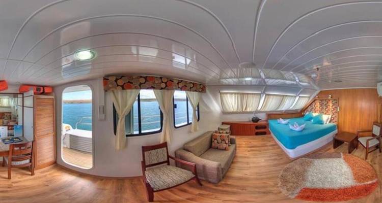 Panoramic interior cabin with large bed, sofa, windows overlooking the sea and wooden flooring.