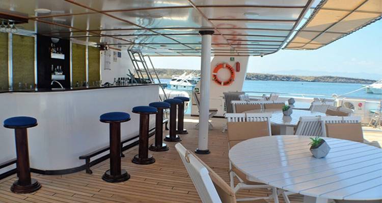 Outdoor bar area on a ship deck with stools, tables and ocean views.