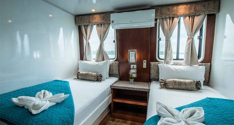 Compact twin cabin with crisp teal bedding, small windows and practical furnishings on a cruise vessel.