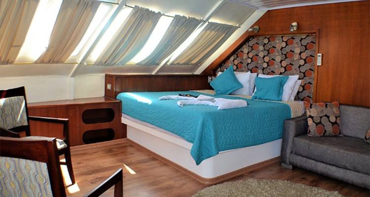 Spacious cabin with angled windows, large bed and seating area bathed in natural light.