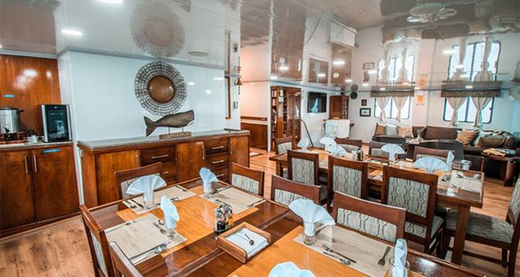 Ship dining room with neatly set wooden tables, napkins and a cozy lounge area.