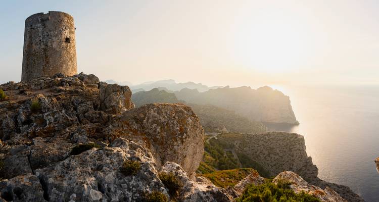 Stone tower on a rocky coastline during sunset.