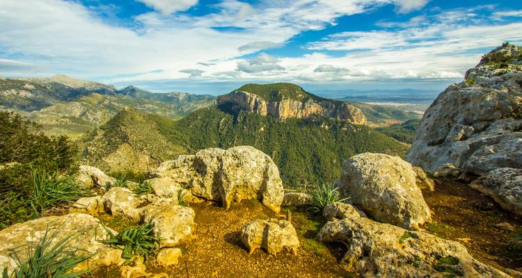 Mountainous landscape with rocky foreground and distant hills under a blue sky.