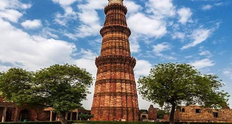 Qutub Minar mit Bäumen im Vordergrund.