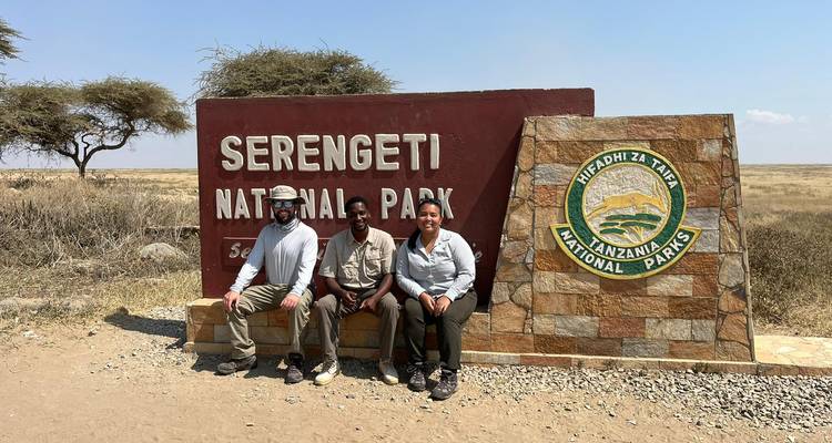 Tourists sitting at the Serengeti National Park sign post.