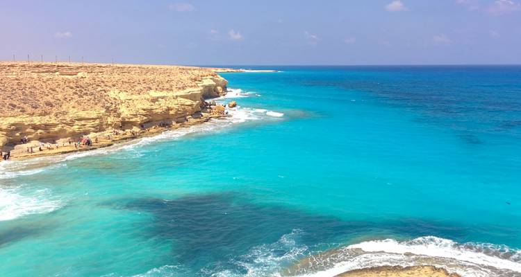 El agua turquesa brillante acaricia los acantilados dorados de piedra caliza en una costa soleada del Mar Rojo.
