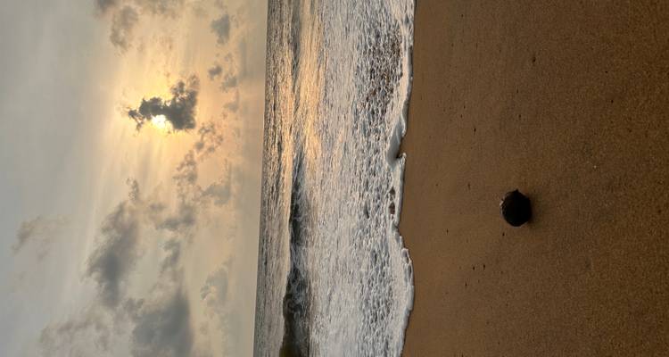 Sandstrand mit einem Sonnenuntergang und Wellen am Ufer.