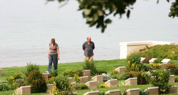 Twee mensen die door een begraafplaats bij het water lopen.