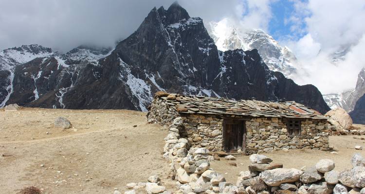 Hutte de pierre avec des montagnes enneigées en arrière-plan.