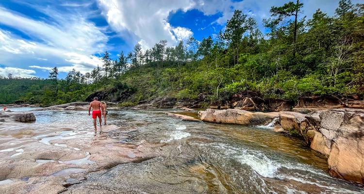 Un joven camina por las aguas poco profundas de piscinas de río cristalinas rodeadas de rocas de granito y bosque de pinos.